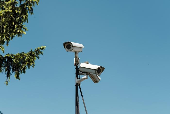 Two security cameras on a pole against a blue sky