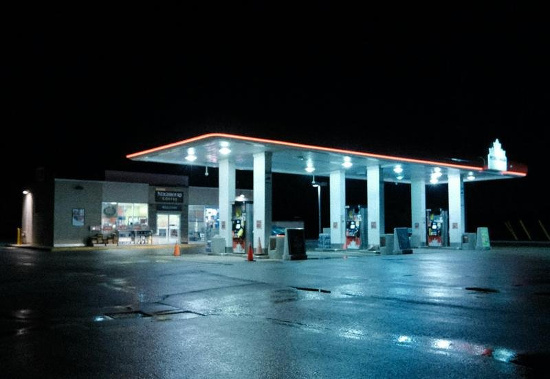 A fuel station canopy glowing at night beside a wet parking lot